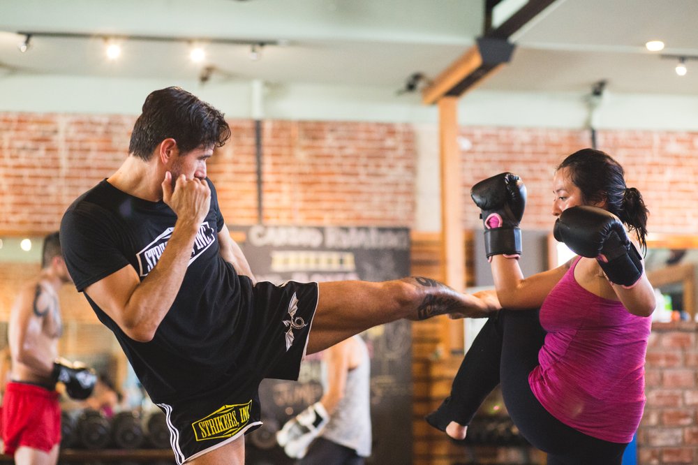 Adult student throwing a Muay Thai kick into pads during class at Strikers Inc.