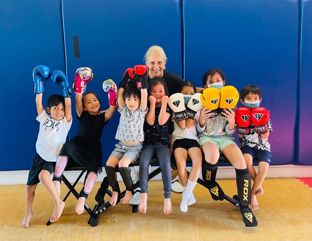 Smiling group of kids holding up boxing gloves after a Strikers Inc. youth class